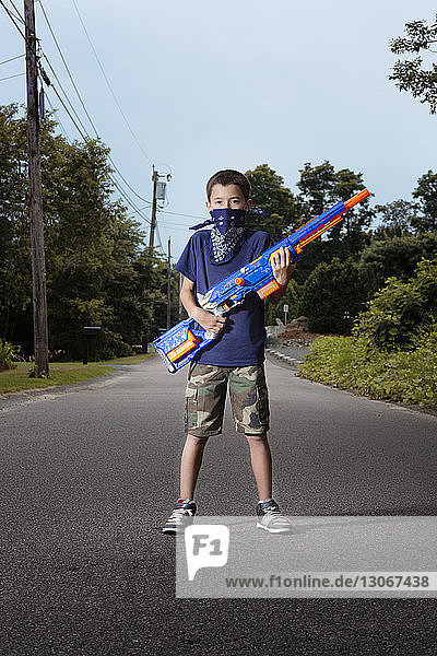 Porträt eines Jungen mit Spielzeugpistole auf Fußweg gegen den Himmel stehend