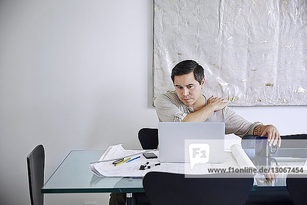Müder Mann hält Schulter bei der Arbeit am Laptop im Büro