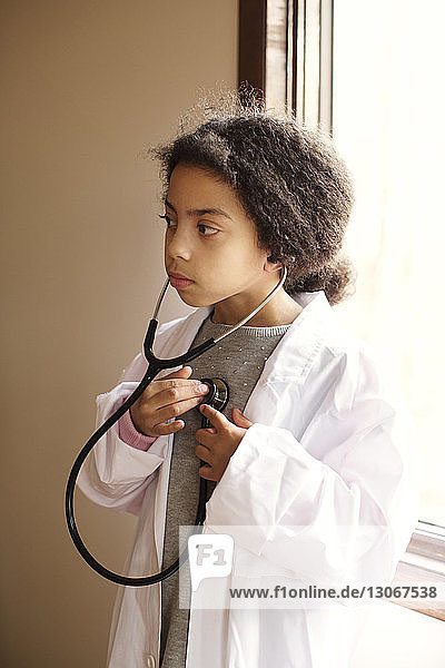 Mädchen im Laborkittel  das zu Hause ihren Herzschlag mit dem Stethoskop hört