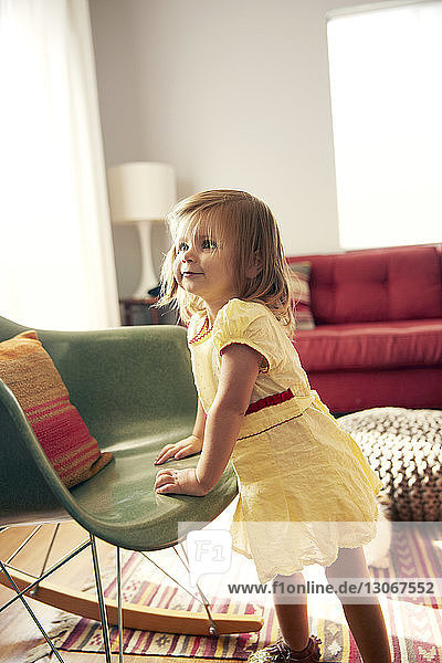 Neugieriges Mädchen schaut weg  während es zu Hause am Stuhl steht
