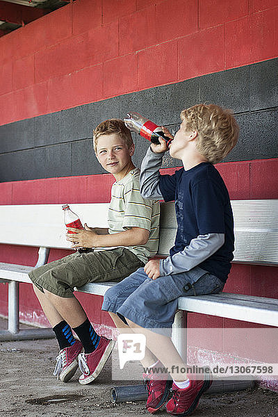 Friends drinking cold drink while sitting at dugout