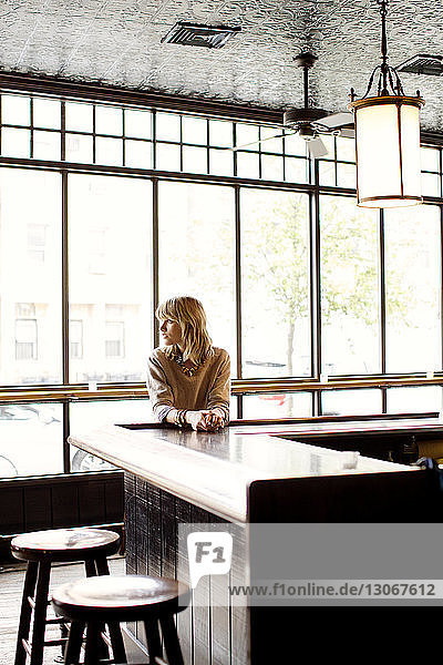 Frau schaut weg  während sie sich an einen Tisch in einer Bar lehnt