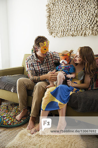 Glückliche Familie mit Maske zu Hause auf dem Sofa sitzend