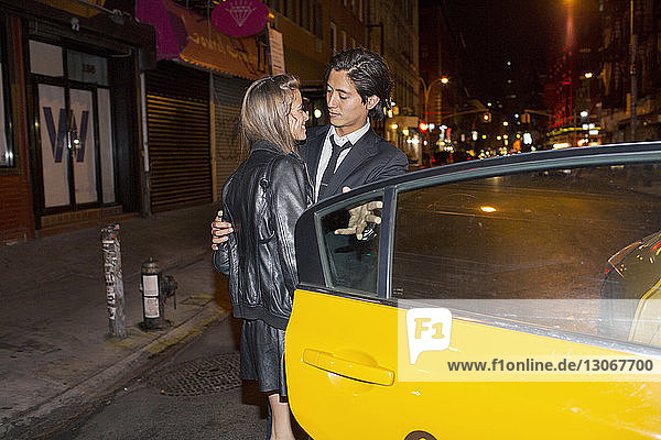 Couple looking at each other while standing by taxi at night