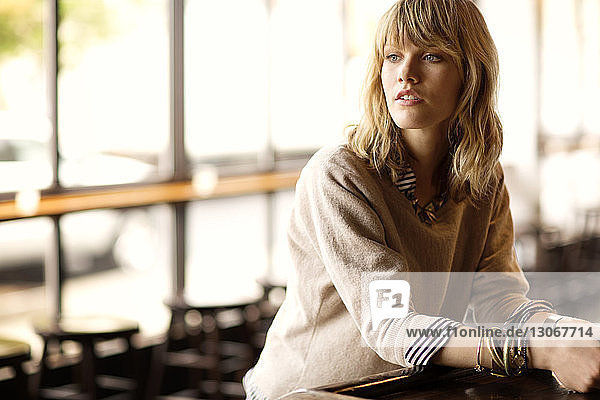 Woman looking away while leaning on table in bar