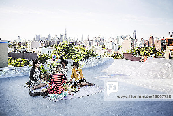 Freunde unterhalten sich beim Essen auf der Terrasse des Gebäudes gegen den Himmel
