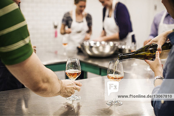Ausgeschnittenes Bild einer Frau  die Wein ausschenkt  während sie in einer Großküche bei ihren Kollegen steht