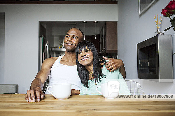 Lächelndes Paar schaut weg  während es zu Hause am Tisch sitzt