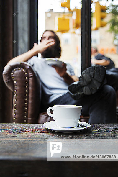 Kaffeetasse auf Tisch mit im Hintergrund sitzendem Mann