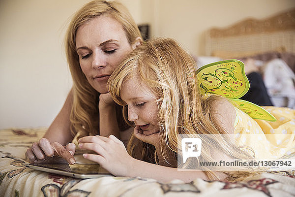 Mädchen mit Mutter benutzt Tablet-Computer  während sie zu Hause im Bett liegen