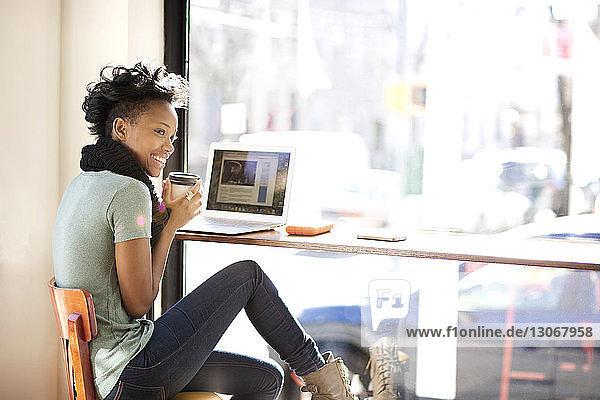 Glückliche Frau trinkt Kaffee  während sie im Café einen Laptop benutzt