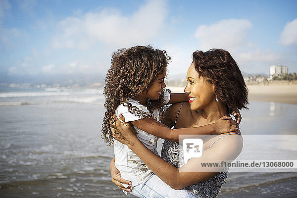 Mutter trägt Tochter  während sie am Strand am Ufer steht