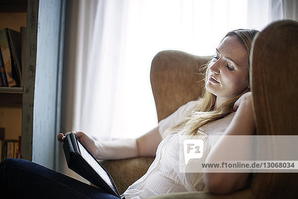 Woman looking at tablet computer while sitting on armchair