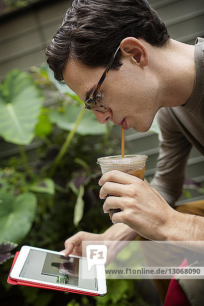 Mann benutzt Tablet-Computer  während er im Hof ein Getränk genießt