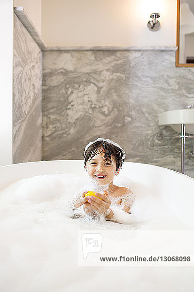 Portrait of boy holding rubber duck while bathing in bathtub