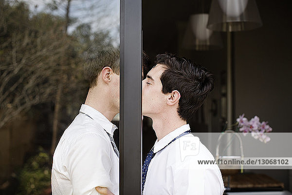 Side view of gay couple kissing while standing at doorway