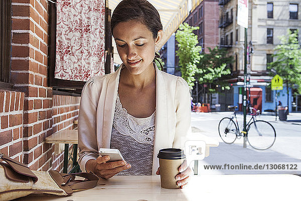 Woman using smart phone while sitting at sidewalk cafe