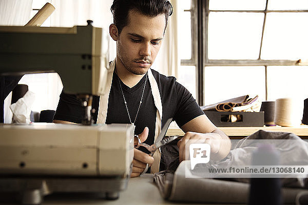Fashion designer cutting gray fabric while working at workshop
