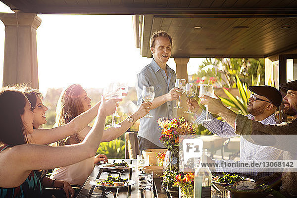 Freunde stoßen bei Tisch auf der Veranda auf Weingläser an