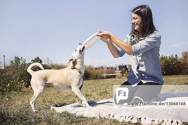 Glückliche Frau schnappt Frisbee von verspieltem Hund im Park gegen den Himmel