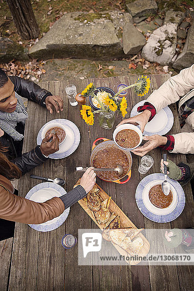 High angle view of woman serving curry to friend at wooden table outdoors