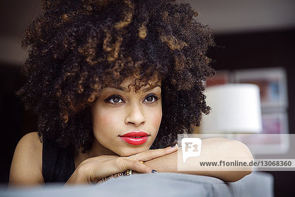 Thoughtful smiling woman with curly hair resting on sofa at home