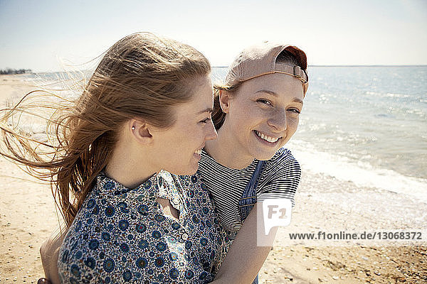 Portrait of happy woman embracing friend while standing at beach