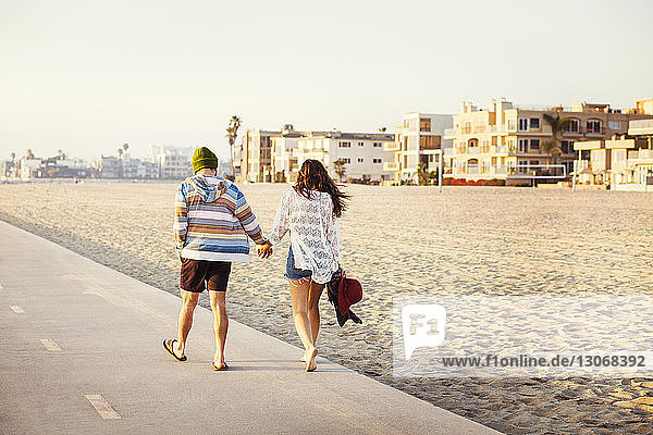 Rear view of couple holding hands and walking at beach on sunny day