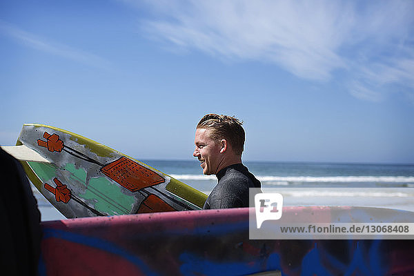 Seitenansicht eines Mannes  der ein Surfbrett trägt  während er gegen das Meer läuft