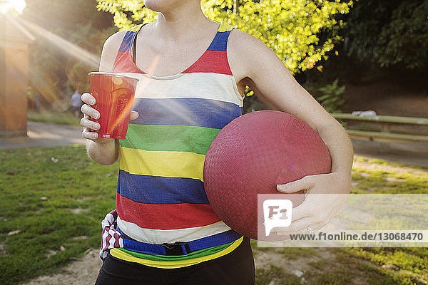 Mittendrin eine Frau  die beim Trinken im Park Völkerball hält