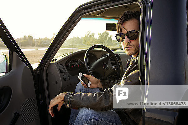 Portrait of man holding smart phone while sitting in car