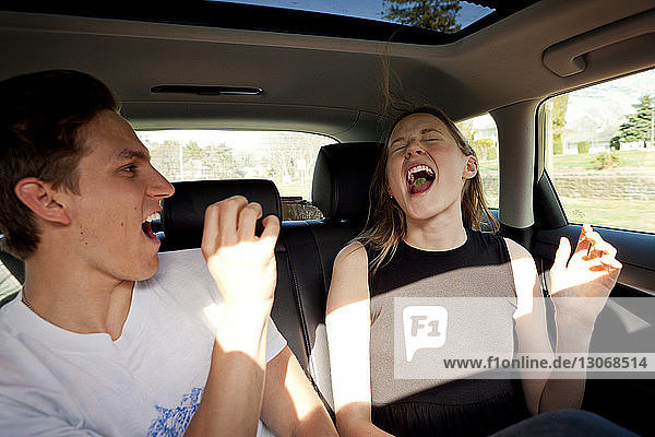Playful man throwing toffee in friends mouth while traveling in car