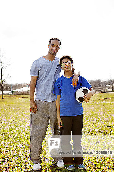 Porträt von Vater und Sohn mit Fussball auf dem Feld vor klarem Himmel stehend