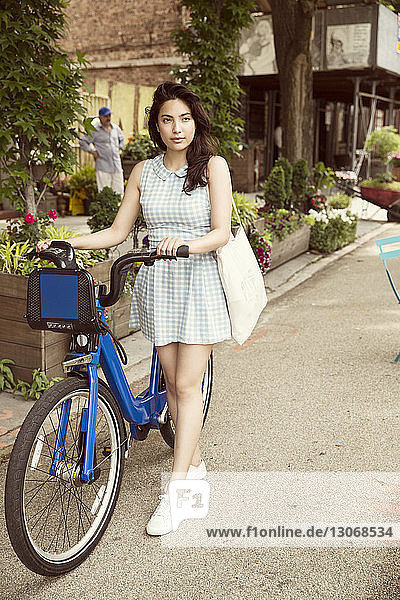 Nachdenkliche Frau mit Fahrrad auf Stadtstraße stehend