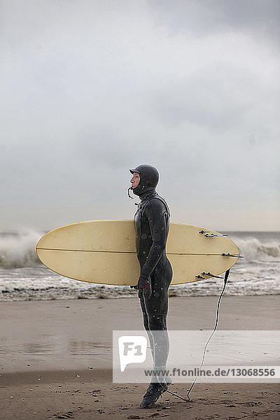 Side view of man holding surfboard while standing at shore