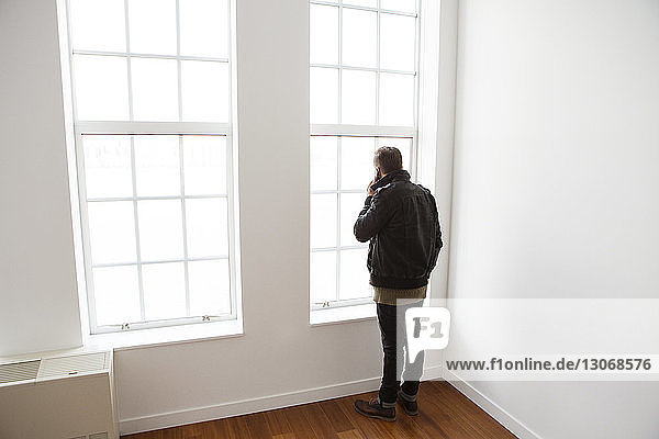 Mann benutzt Mobiltelefon  während er mit seinem Sohn zu Hause am Fenster sitzt