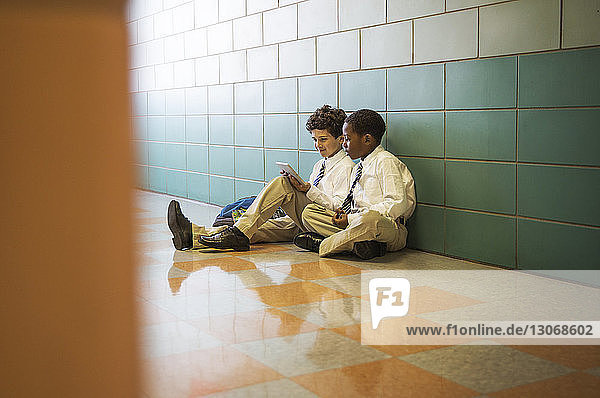 Boys using tablet computer while sitting on floor in corridor