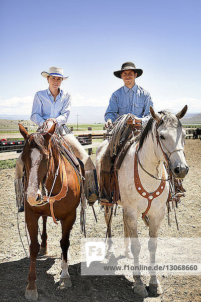 Porträt eines Mannes und einer Frau  die auf Pferden auf einer Ranch gegen den Himmel sitzen