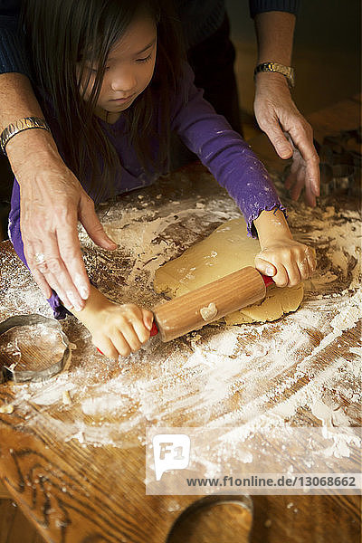 Schrägansicht eines Mädchens mit einer Großmutter  die Teig für die Zubereitung von Keksen rollt