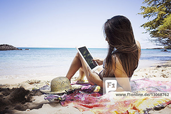 Woman using tablet computer while sitting at shore