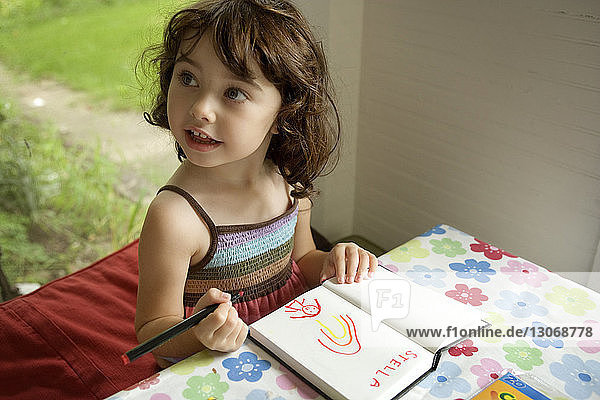 Mädchen schaut beim Zeichnen am Tisch zu Hause weg