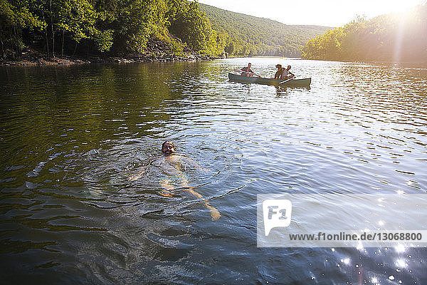 Mann schwimmt  während Freunde im Kanu sitzen