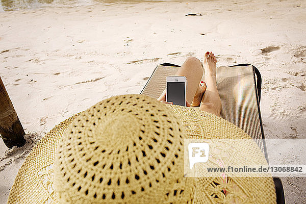 High angle view of woman using smart phone while relaxing on lounge chair at beach
