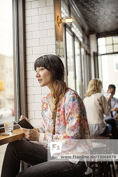 Woman with small book looking away while sitting in bar