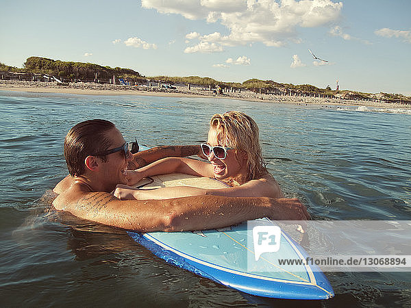 Couple leaning on surfboard at beach
