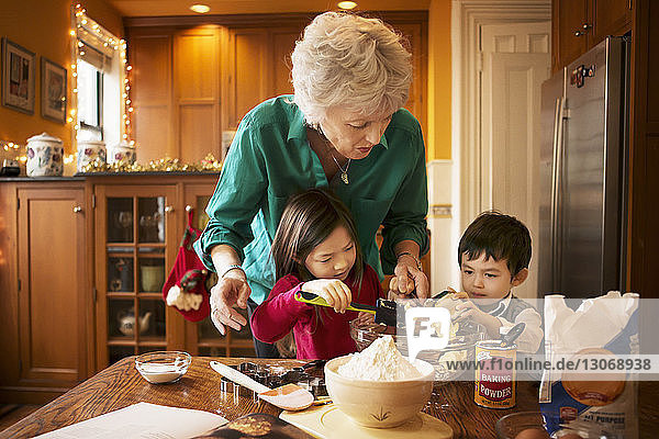 Kinder  die Butter in einer Schüssel porieren  während sie zu Hause mit der Großmutter zu Weihnachten Kekse backen