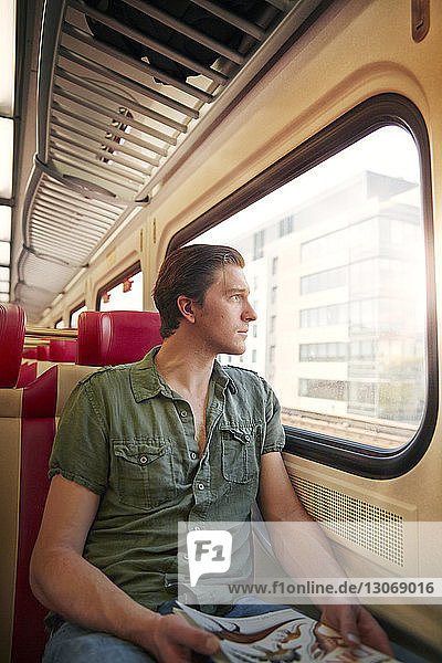 Nachdenklicher Mann schaut durch Fenster  während er im Zug reist