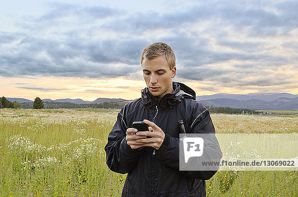 Mann benutzt Smartphone  während er auf dem Feld vor bewölktem Himmel steht