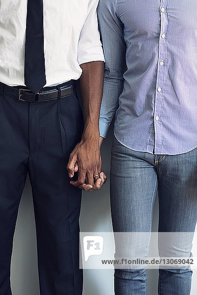 Mittelsektion eines schwulen Paares  das sich an der Wand stehend an der Hand hält
