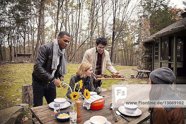 Men serving food to friends sitting at table against trees